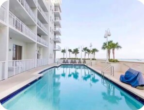 Une piscine avec vue sur l’océan, entourée d’un bâtiment blanc doté de balcons.