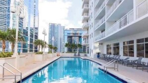 A swimming pool with a view of high-rise buildings, sun loungers, and a clear sky. - Bay View Condo 18th floor with free parking (Miami)