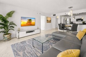 Ein modernes Wohnzimmer mit einer Couch, einem Glastisch und einem Flachbildfernseher auf einer weißen Unterhaltungsanlage.