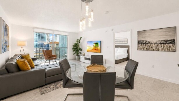 A modern living room with a glass dining table, leather sofa, and a city view. - Bay View Condo 18th floor with free parking (Miami)