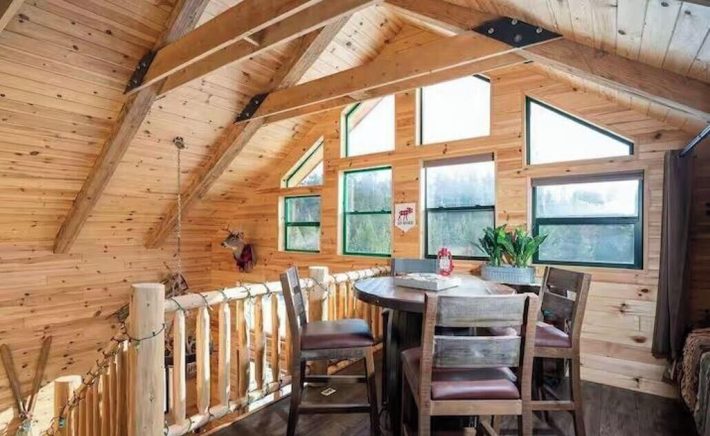 A wooden interior with a high ceiling, multiple windows, and a dining area with chairs and a table.