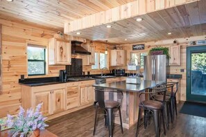 A modern kitchen with wooden cabinetry, a central island with bar stools, and a large window providing natural light.