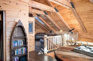 A cozy wooden interior with a loft bed, a bookshelf, and a dining table.