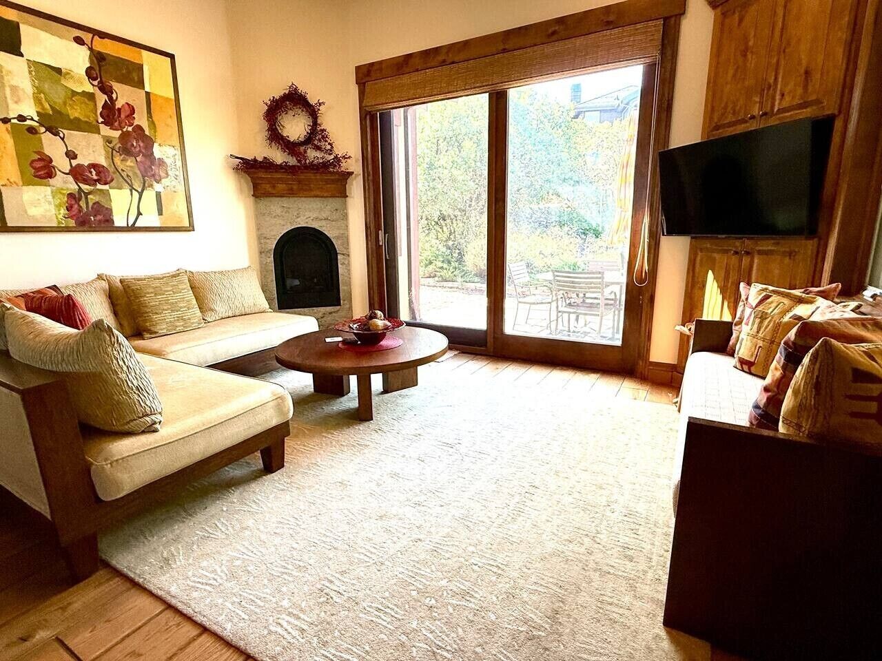 Een woonkamer met een open haard, een aan de muur bevestigde televisie en een groot raam met uitzicht op de omgeving.