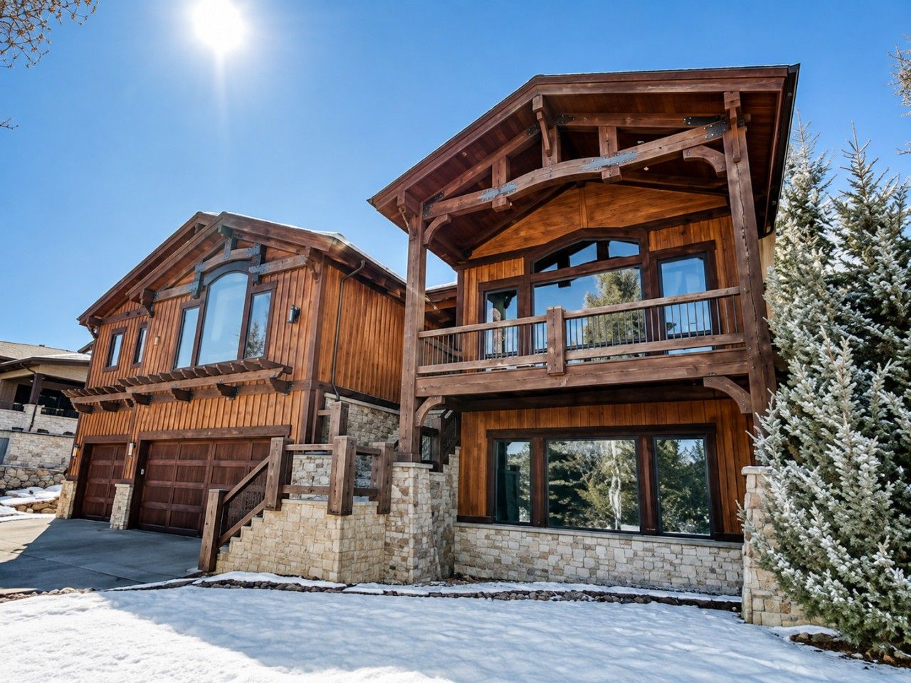 A two-story wooden cabin with a stone foundation, large windows, and a balcony.