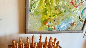 A chessboard with wooden pieces on a table, a framed abstract painting on the wall, and a carpeted floor. - Deer Valley Luxury Lodge | Shuttle, Hot Tub, Games (Park City)