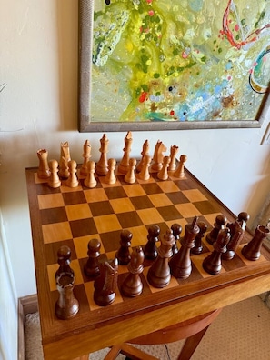 Ein Schachbrett mit hölzernen Figuren auf einem Tisch, ein gerahmtes abstraktes Gemälde an der Wand und ein Teppichboden.