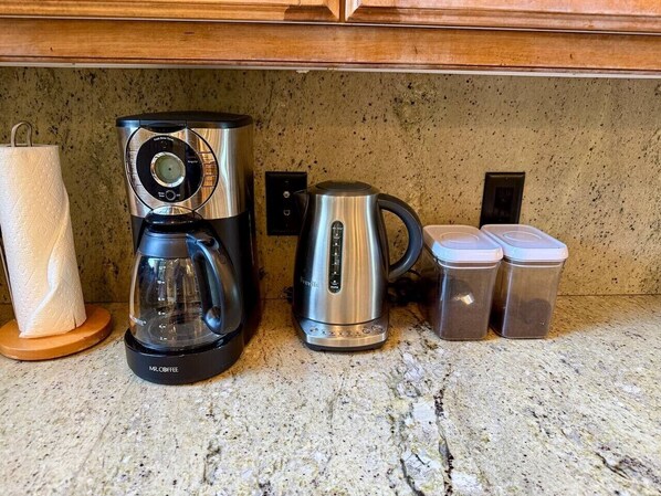Un plan de travail de cuisine avec une machine à café, une bouilloire et deux récipients.