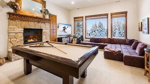 A pool table with a stone fireplace, a sectional sofa, and a television in a living room. - Deer Valley Luxury Lodge | Shuttle, Hot Tub, Games (Park City)