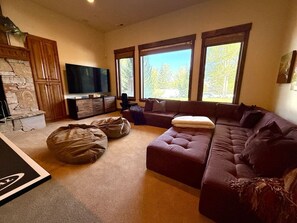 Ein Wohnzimmer mit Ecksofa, zwei Sitzsäcken, einem Flachbildfernseher und einem Kamin aus Stein.