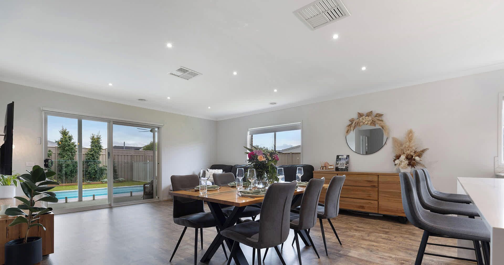 A dining area with a table set for four, a sofa, and a view of a swimming pool.