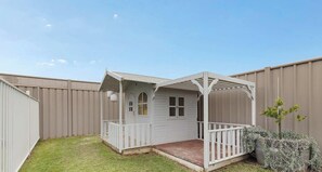 Ein weißes Spielhaus mit Veranda, umgeben von einem eingezäunten Garten.