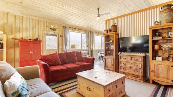 A cozy living room with a red sofa, wooden cabinets, a television, and a large window.