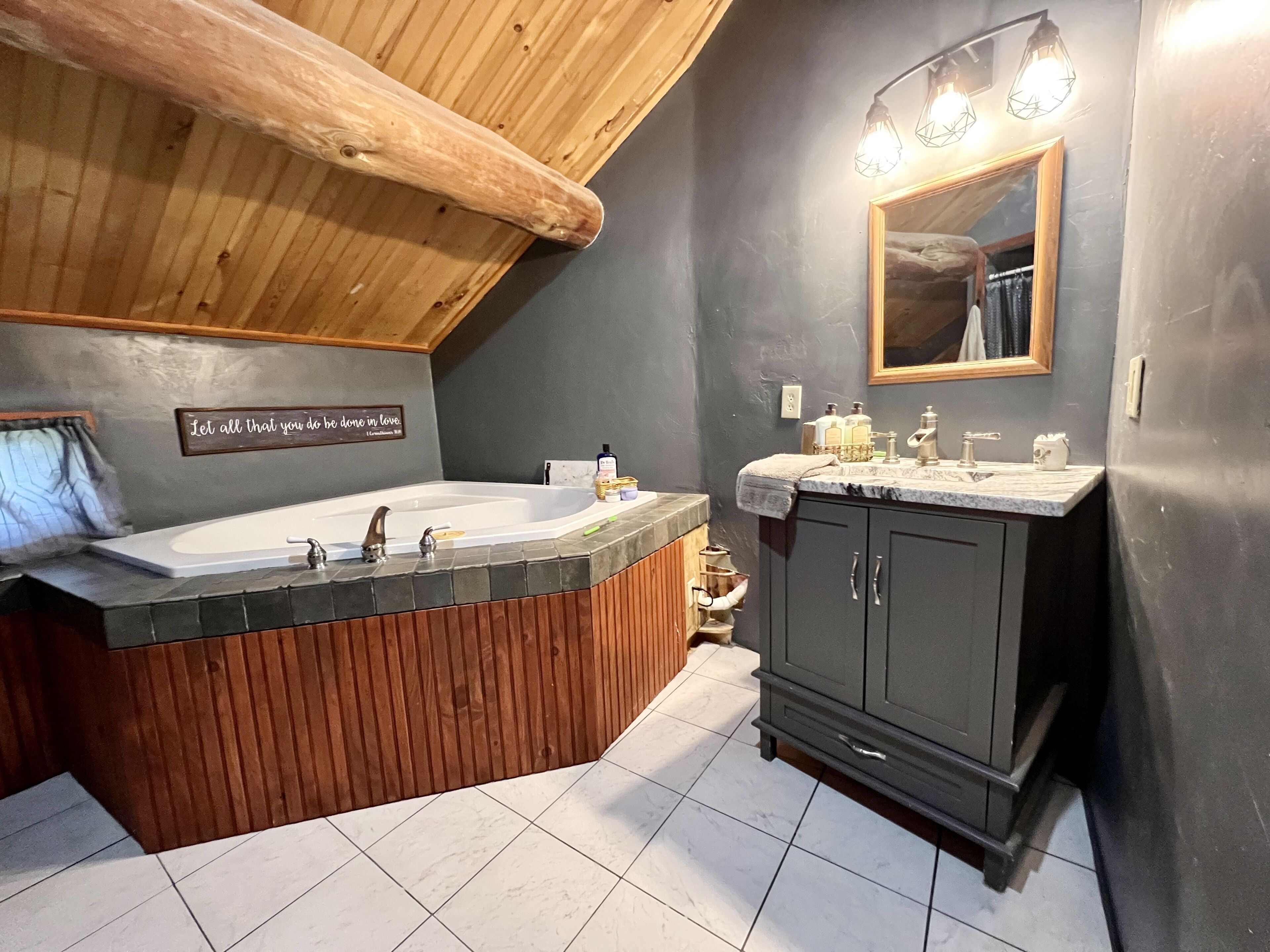 A bathroom with a wooden vanity, a large bathtub, and a mirror with lights.