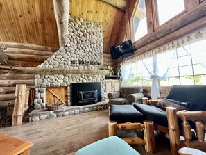 A log cabin interior with a stone fireplace, wooden furniture, and a television mounted on the wall. - Gorgeous Custom Built Log Home w/ Indoor Pool (Annsville)