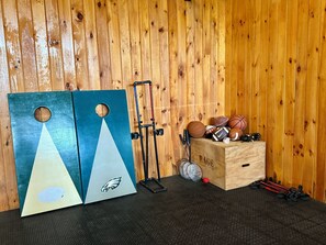 A room with a wooden wall, a blue and white object with an eagle logo, a rack with sports equipment, and a wooden box with sports balls. - Gorgeous Custom Built Log Home w/ Indoor Pool (Annsville)