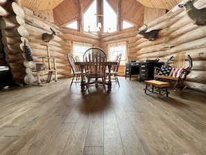 A log cabin interior with a wooden dining table, chairs, a rocking chair with an American flag cushion, and a fireplace. - Gorgeous Custom Built Log Home w/ Indoor Pool (Annsville)