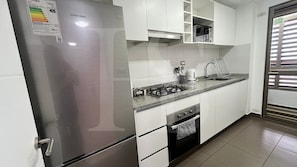 Una cocina con refrigerador de acero inoxidable, estufa a gas, microondas y gabinetes blancos.