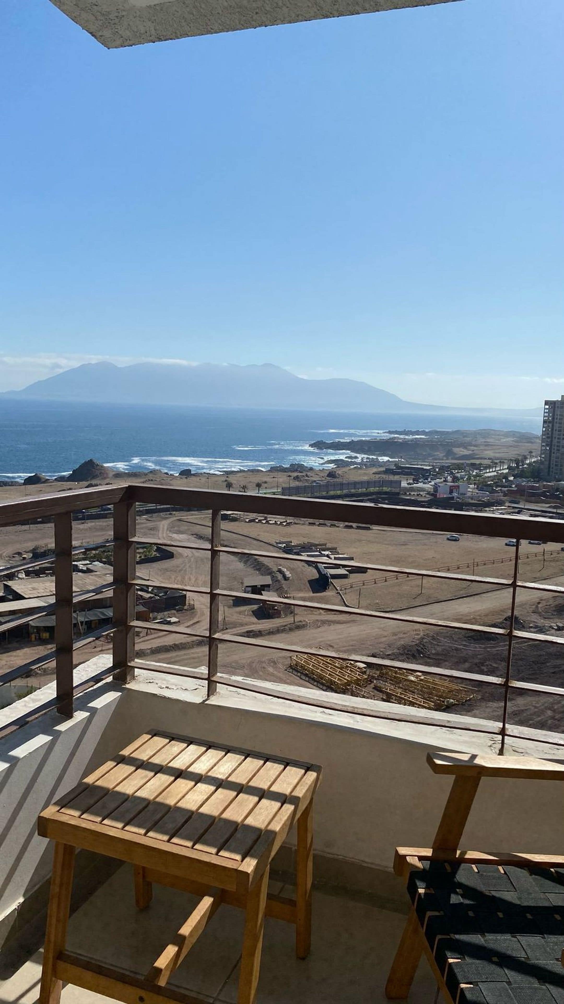 A balcony with a view of a beach, a mountain, and a parking lot.
