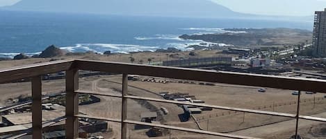 A balcony with a view of a beach, a mountain, and a parking lot.