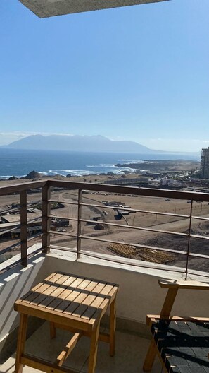 A balcony with a view of a beach, a mountain, and a parking lot.
