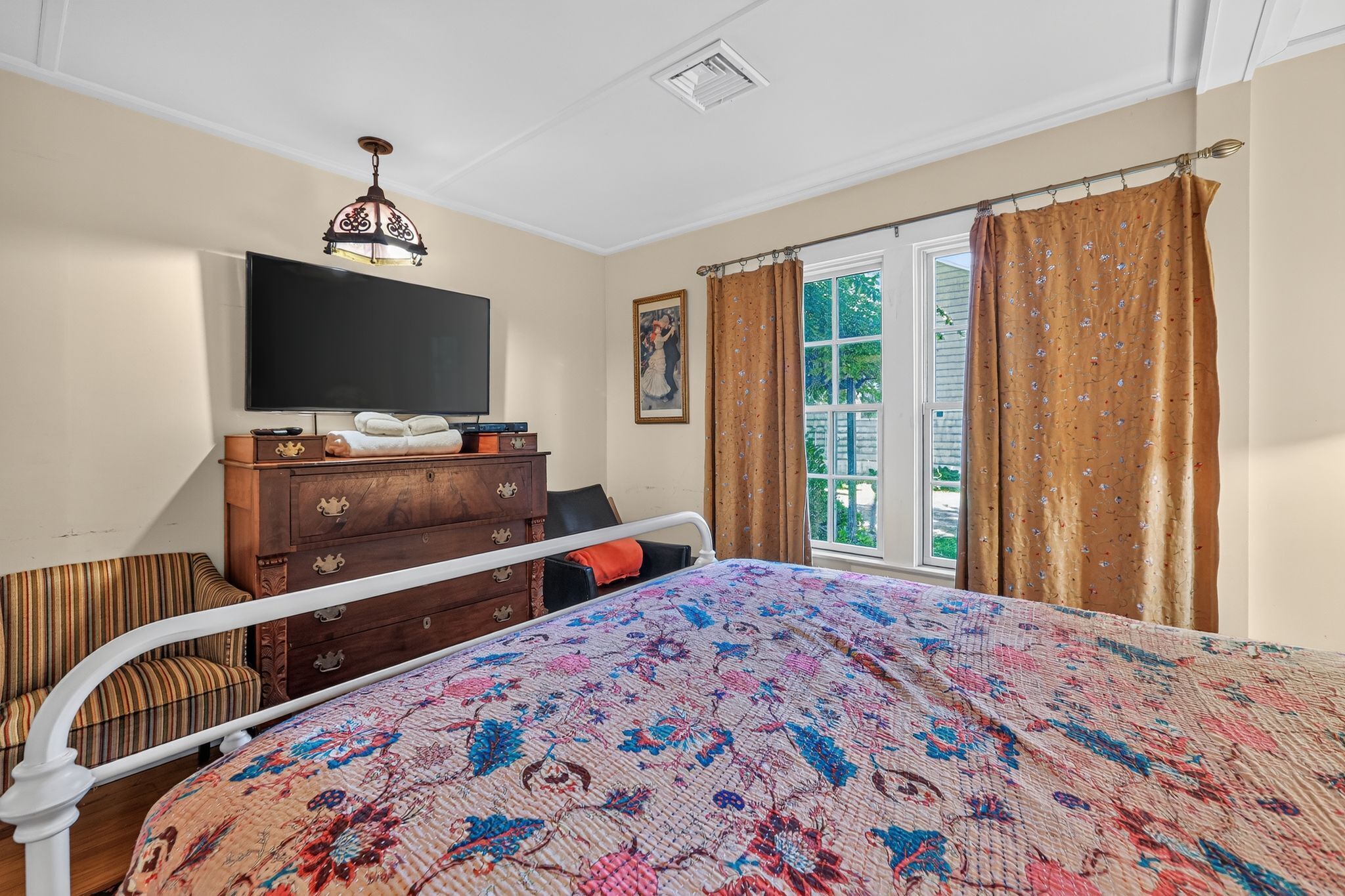 A bedroom with a bed, a dresser, a television, and a window with curtains.