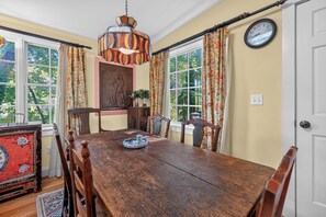 A dining room with a wooden table, chairs, a chandelier, and a clock on the wall.