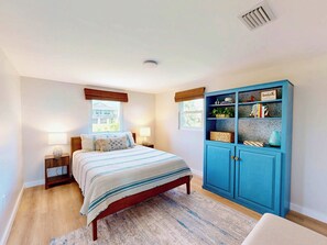 A bedroom with a bed, bedside lamps, a window, a blue cabinet with shelves, and a view of a building outside. - Wake up to ocean breezes! (St. Augustine)