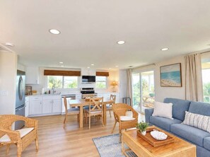 A modern kitchen with white cabinets, a dining area with wooden furniture, and a living room with a blue sofa and wicker chairs. - Wake up to ocean breezes! (St. Augustine)