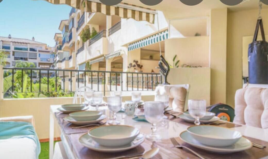 A dining area with a table set for two, a view of the building's exterior, and a balcony with a railing.