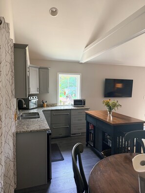 Cocina compacta con microondas integrado, horno y pileta. Hay un comedor con una mesa y sillas de madera.