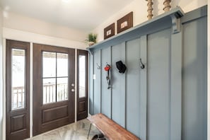 Ein Flur mit einer hölzernen Bank, einer blauen Wand mit Haken und einer Tür mit Glasfeldern.