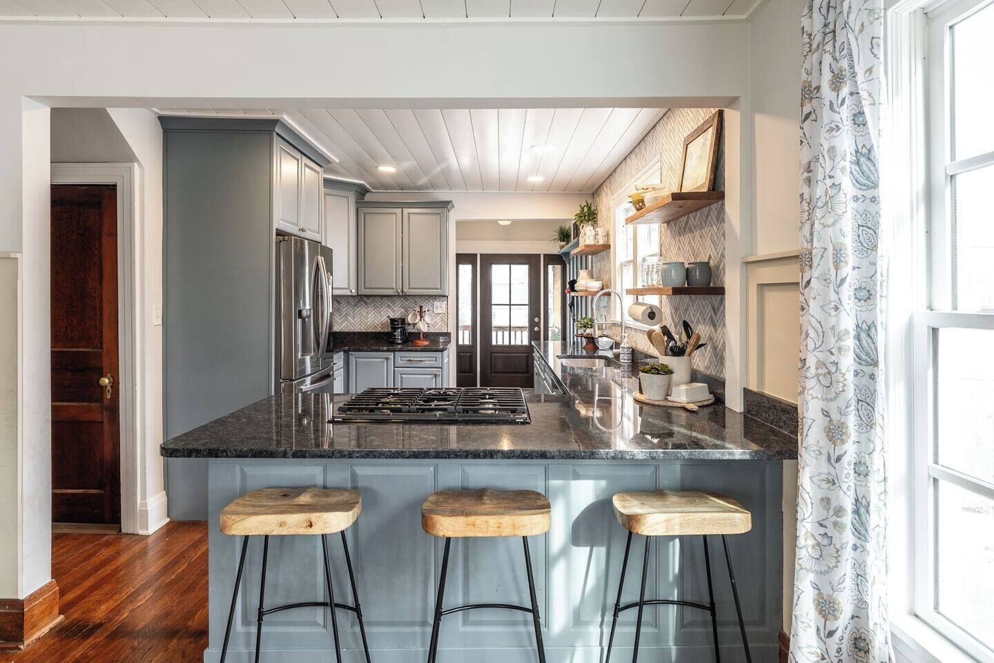 A kitchen with a central island, wooden stools, and a refrigerator.