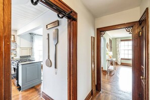 A hallway with a wooden door, a measuring tape, and a kitchen area with a stove and cabinets.