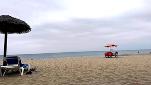 A beach with a thatched umbrella, a red beach cart, and a blue lounge chair. - Apartment in Punta Centinela Townhouse 200 (Santa Elena)
