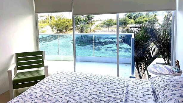 A bedroom with a bed, a chair, and a view of a swimming pool and greenery. - Apartment in Punta Centinela Townhouse 200 (Santa Elena)