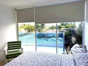 Ein Schlafzimmer mit Bett, einem Sessel und Blick auf einen Pool und Grünflächen.