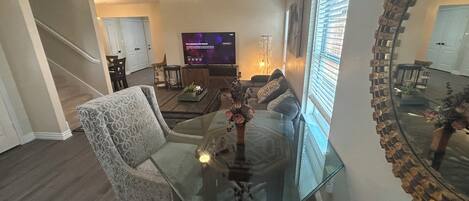 Ein Wohnzimmer mit Glastisch, gemusterten Sofas, Fernseher und Deckenventilator.