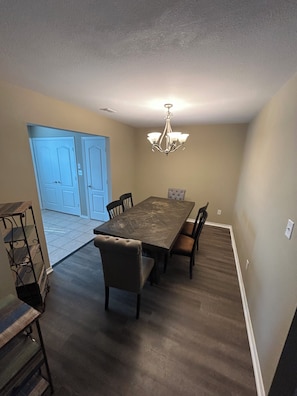 A dining area with a rectangular table, six chairs, a chandelier, and a door in the background.