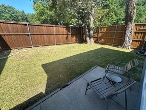 Ein Garten mit Holzzaun, einem Baum und einer Terrasse mit einem Metalltisch und Stühlen.