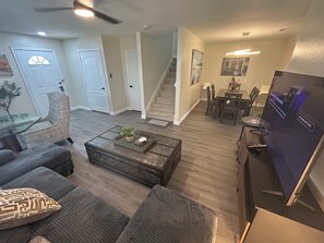 A living room with a sofa, coffee table, and a television. There is a staircase leading to another room.