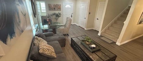 Una sala de estar con sofá, sillones, una mesa de centro de vidrio y una escalera.