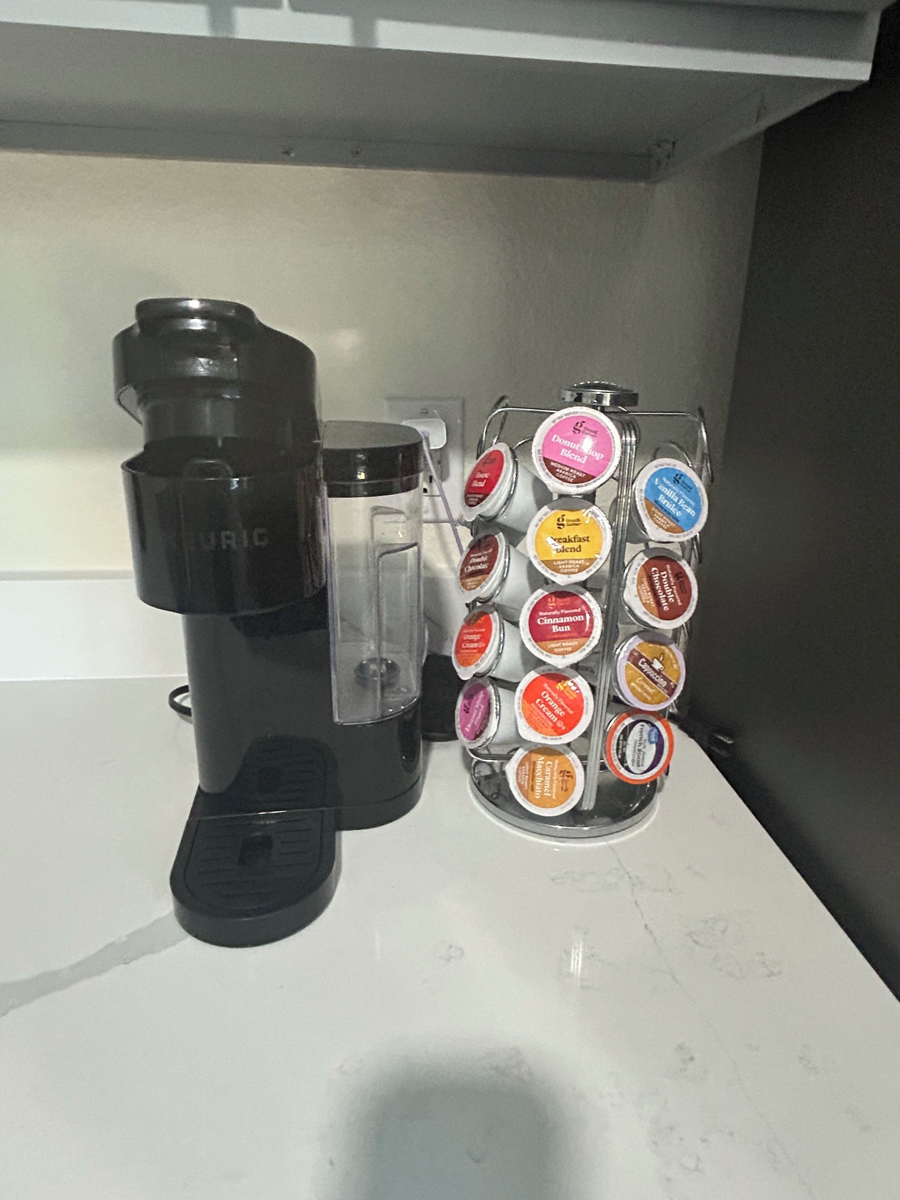 A coffee machine and a coffee pod holder with various flavors on a countertop.
