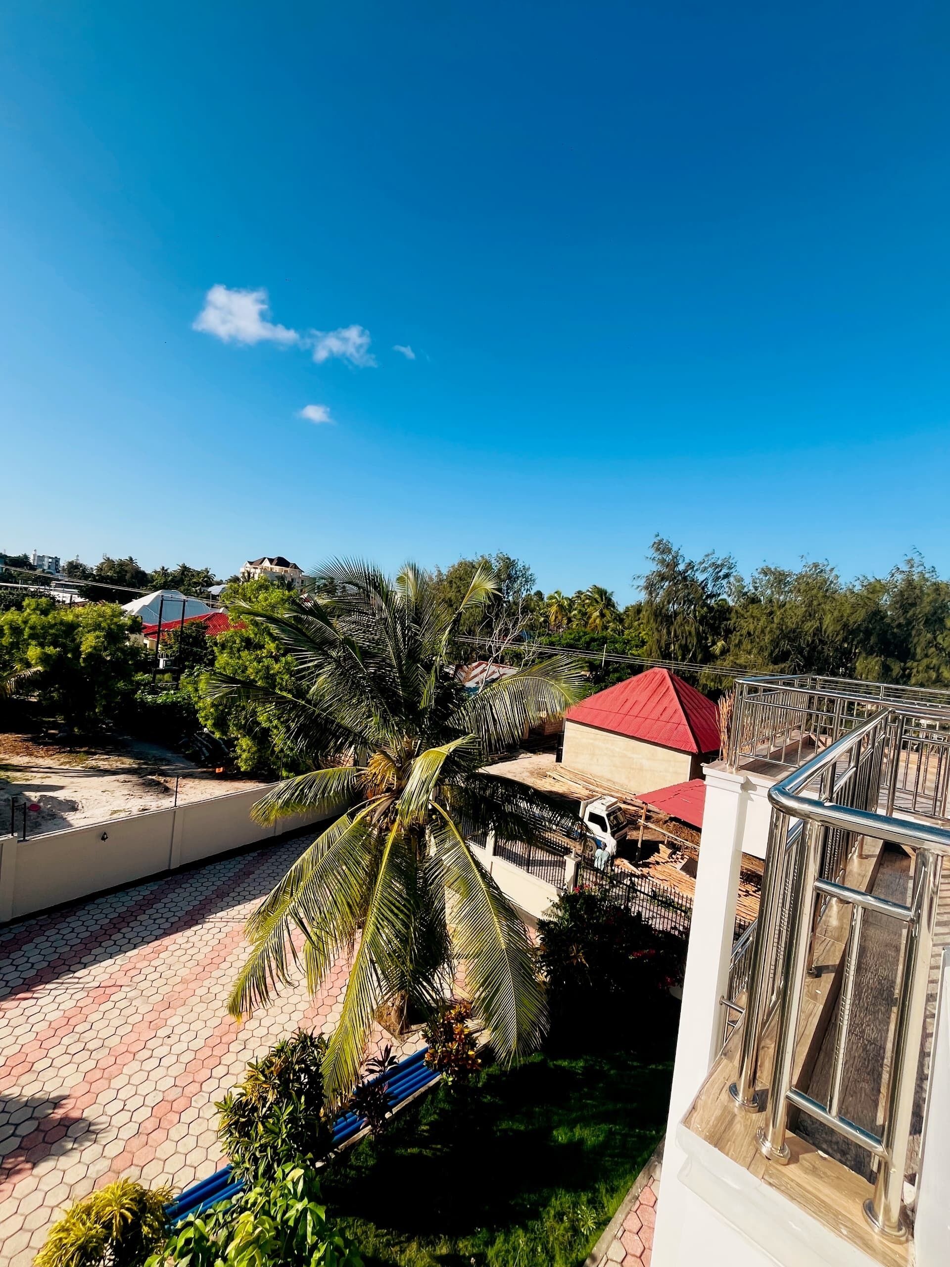 A residential area with a paved walkway, palm trees, and a building with a red roof.