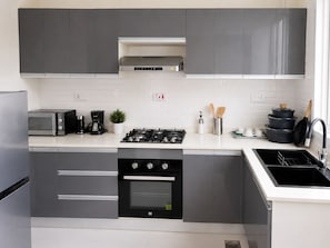A modern kitchen with grey cabinets, a built-in oven, a gas stove, a microwave, and a coffee maker. - Palm Residence retreat in Paje (Paje)