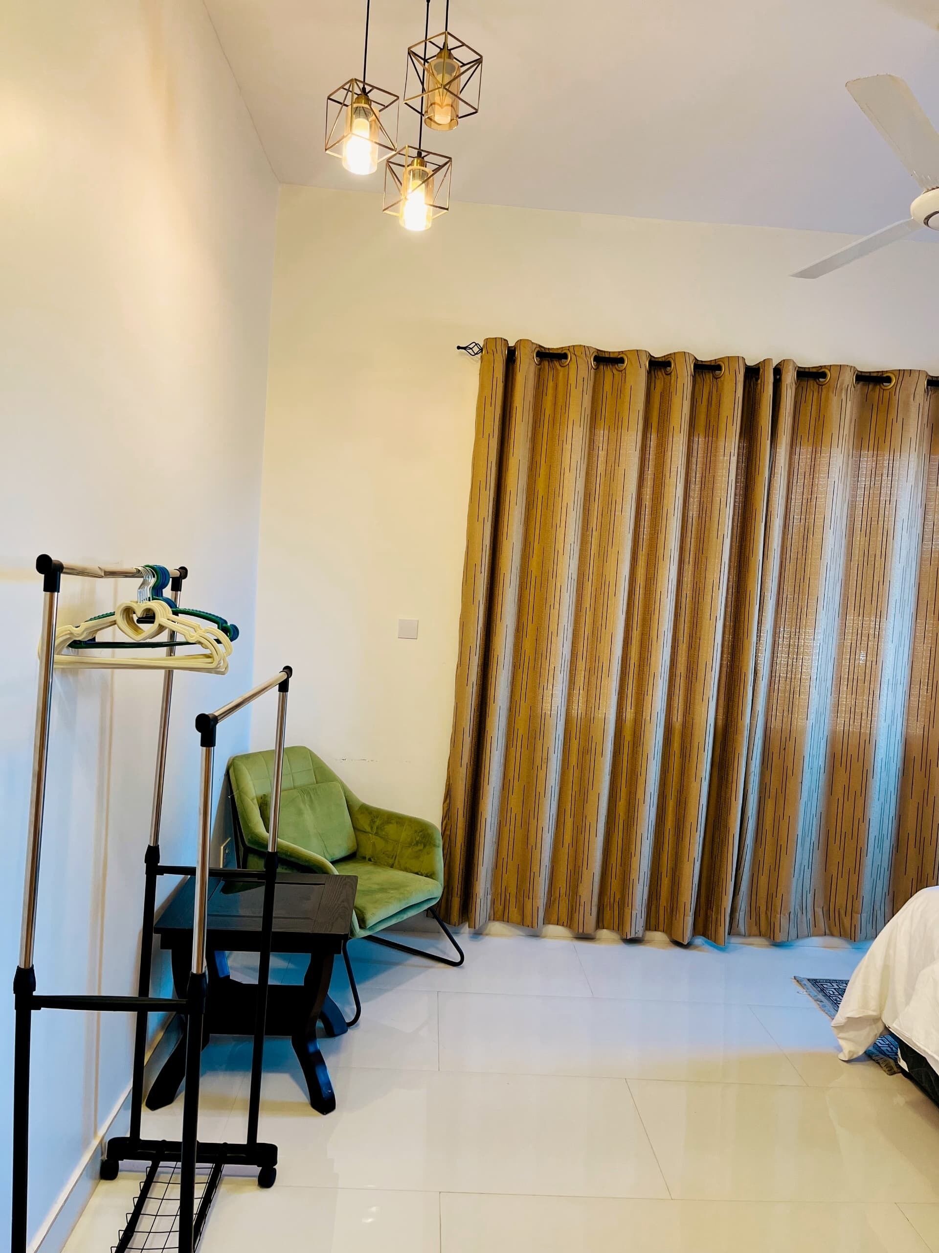 Ein Zimmer mit einem grünen Sessel, einem Bett, einem Deckenventilator und einem Vorhang.