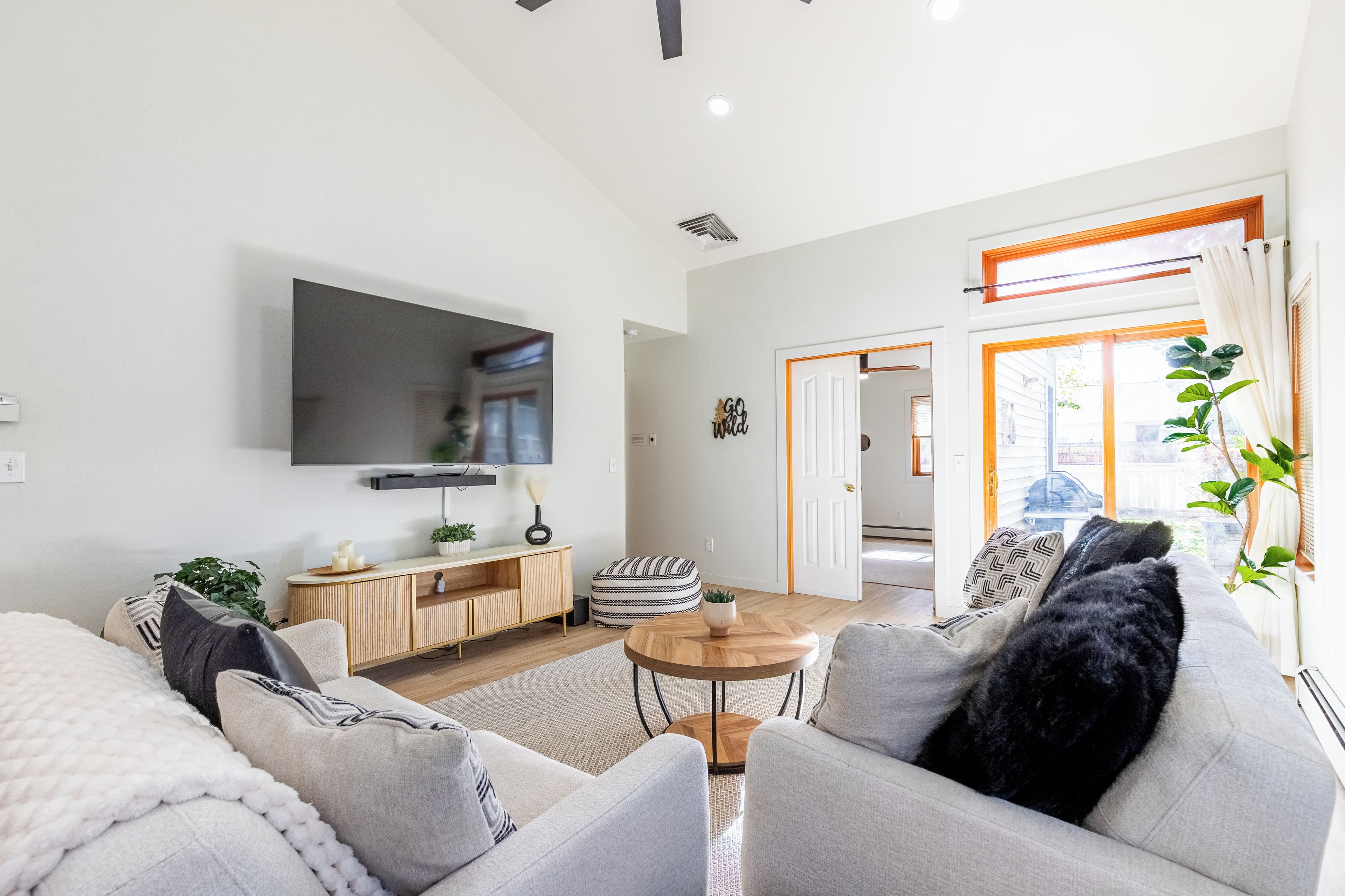 A modern living room with a flat-screen TV, a wooden cabinet, a round coffee table, and a sofa with cushions.