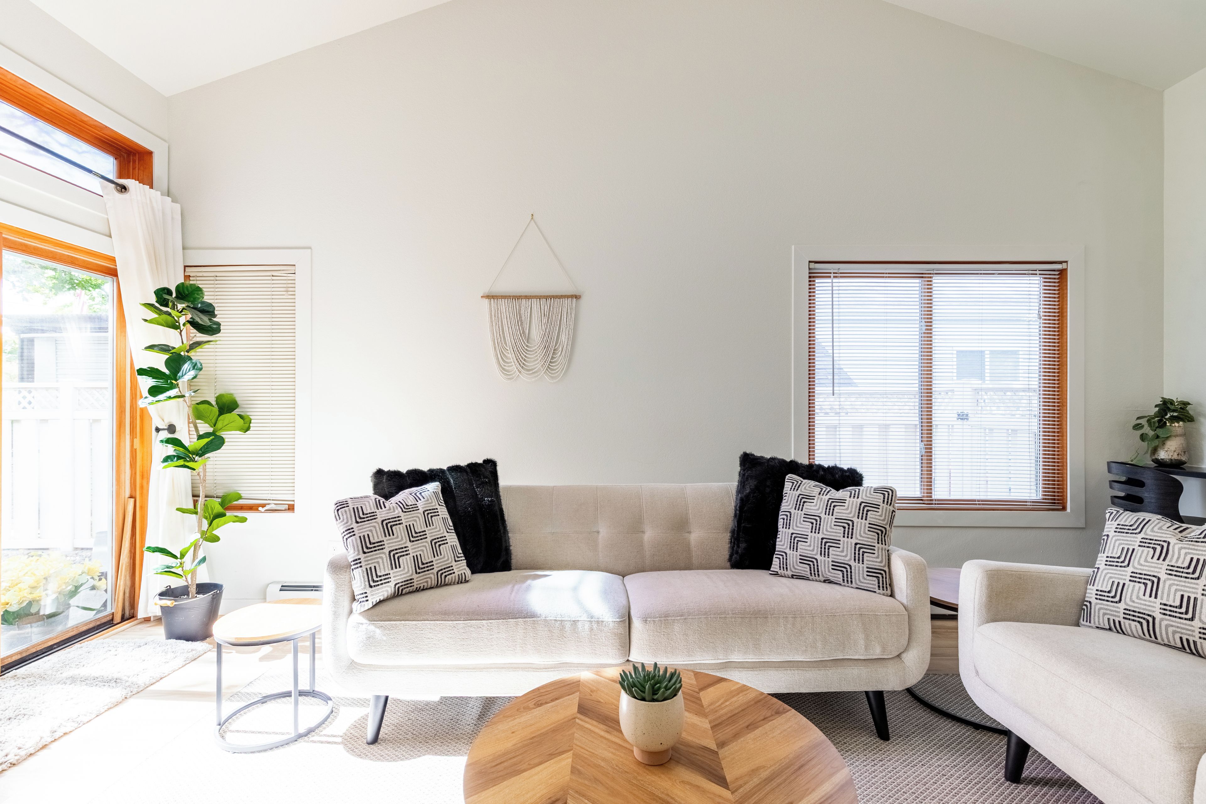 A modern living room with a beige sofa, two armchairs, a coffee table, and a hanging macrame wall decoration.