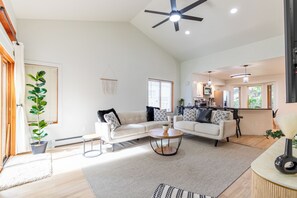 A spacious living room with a high ceiling fan, a kitchen area with modern appliances, and a dining space with a round table. - Modern, pet-friendly Retreat near everything! (Montrose)