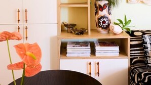 Une pièce avec un meuble en bois, des étagères remplies de livres et d’objets décoratifs, un vase avec des fleurs et un canapé à motifs noir et blanc.